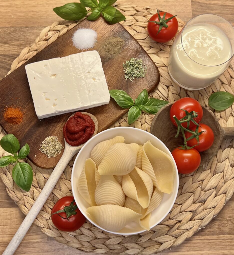 Zutaten für Tomate-feta-Pasta: Tomaten, Tomatenmark, Basilikum, Sahne, Gewürze, Nudeln, Holzuntergrund mit runder Flechtmatte drauf
